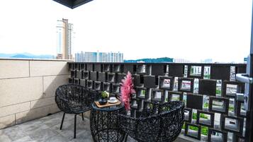 A balcony with two black wicker chairs, a small round table with a plant and a cup, and a decorative pink plant.