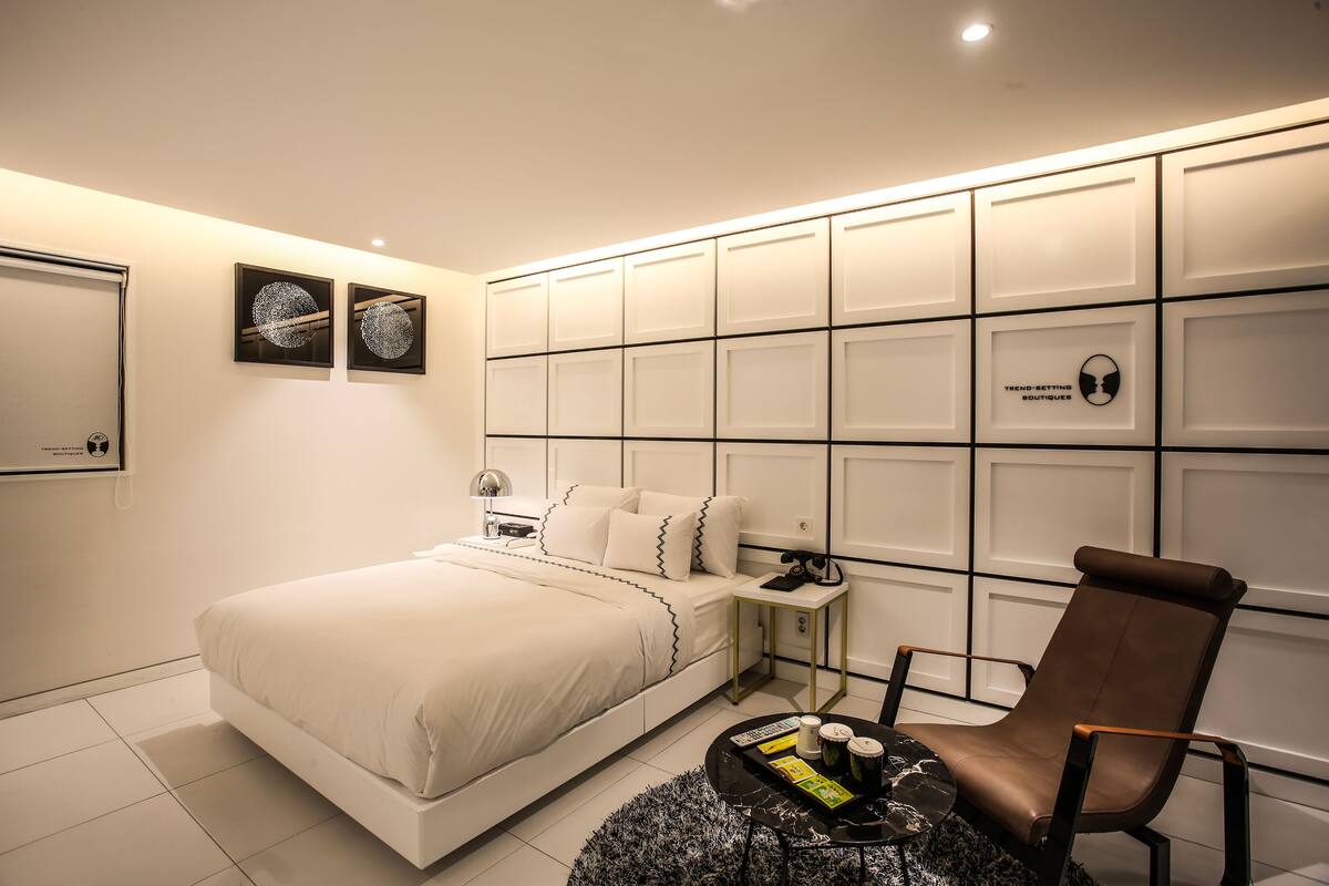 A modern bedroom with a large bed, a nightstand, a chair, and a wall with storage compartments.
