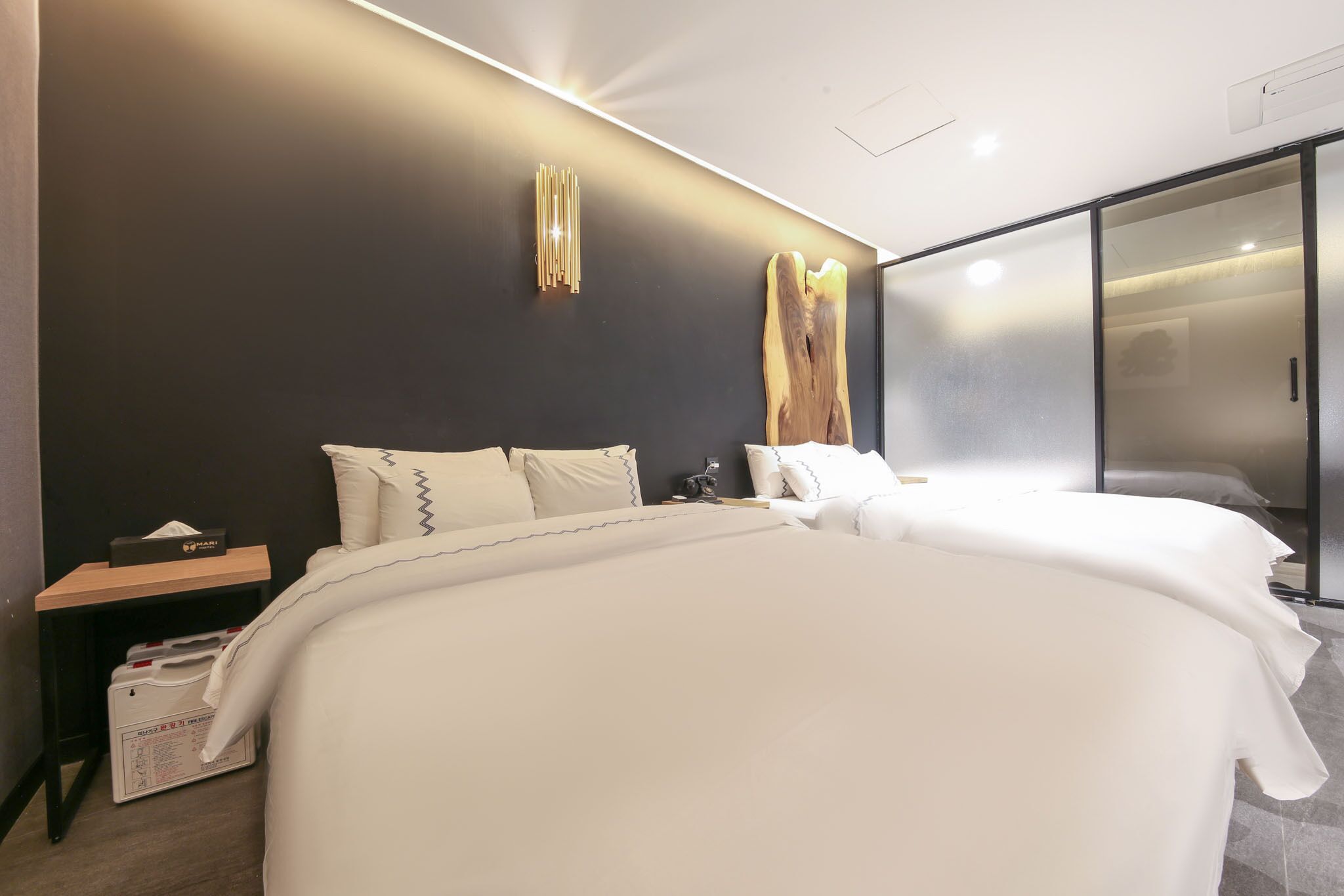 Ein modernes Hotelzimmer mit einem großen Bett, einem Nachttisch mit Taschentuchbox und einem Beistelltisch ebenfalls mit Taschentuchbox und Taschentüchern.