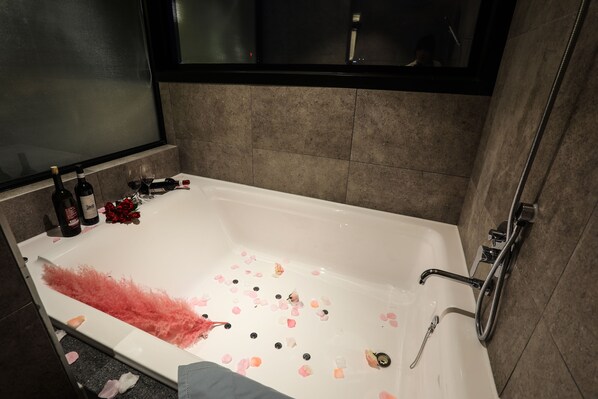 A bathroom with a bathtub, rose petals, and wine bottles. - Jeonju Mari Hotel Terminal Store (Jeonju)