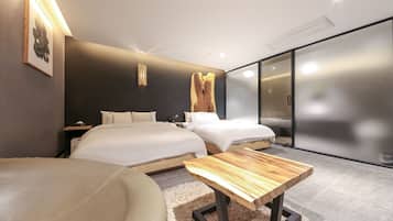 Una habitación de hotel moderna con dos camas, una mesita de madera, un sofá y un ventanal con vistas.