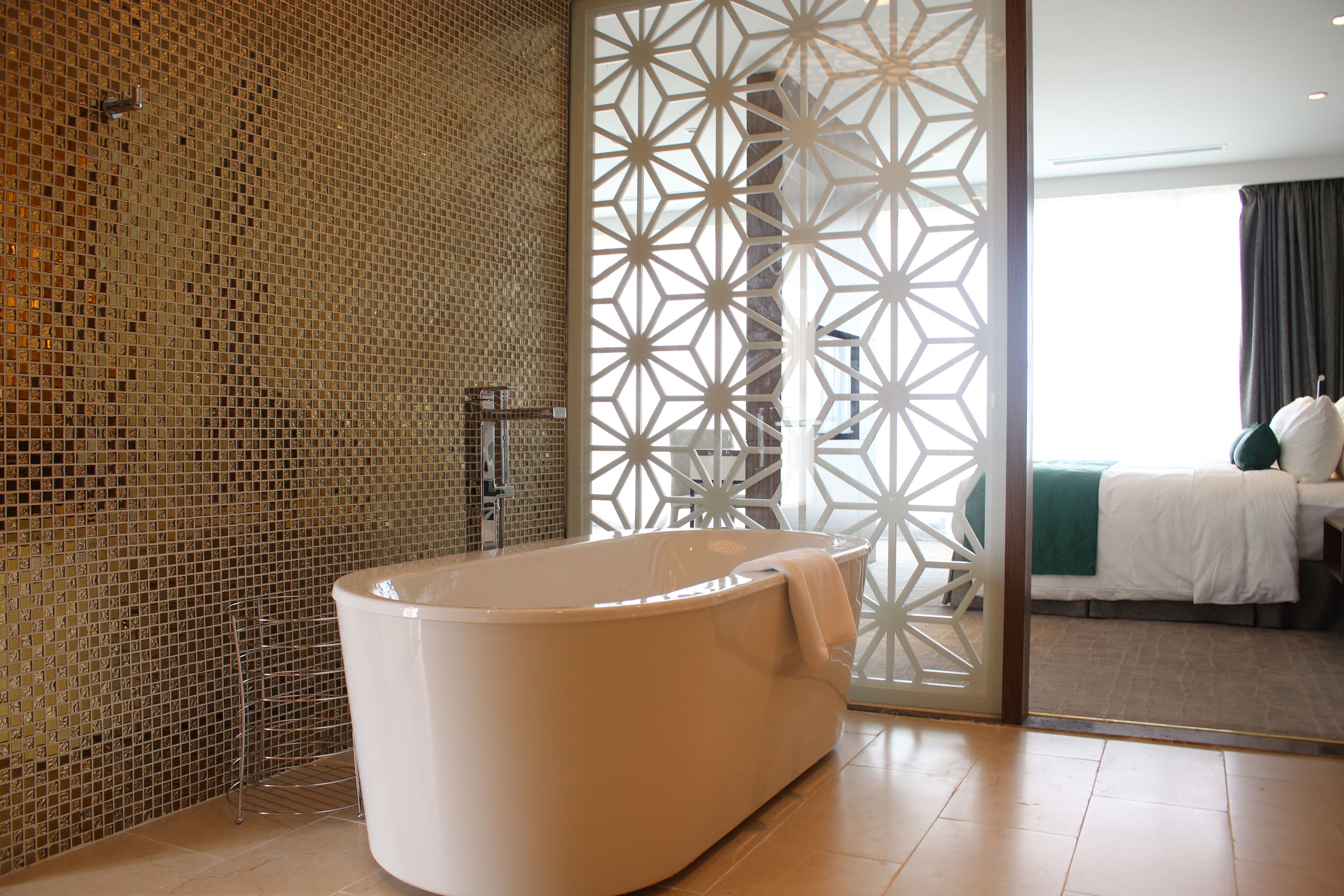 Ein modernes Badezimmer mit einer freistehenden Badewanne, einer mosaikverzierten Wand und Blick in ein Schlafzimmer durch eine geteilte Wand.