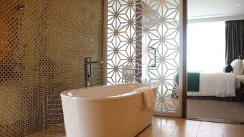 A modern bathroom with a freestanding bathtub, a mosaic wall, and a view of a bedroom through a patterned partition.