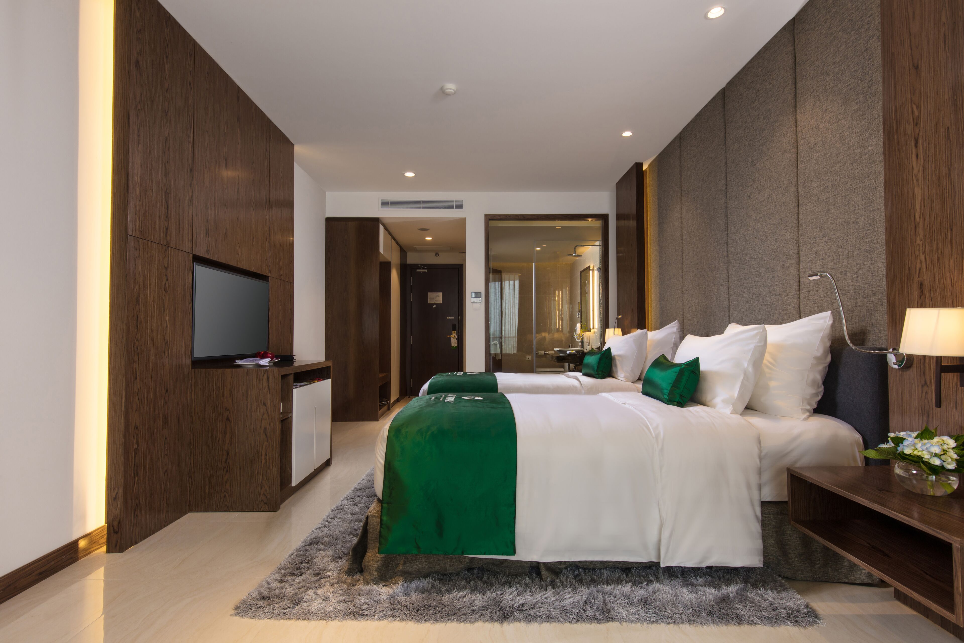 Una habitación de hotel moderna con dos camas, un televisor de pantalla plana, un escritorio y un espejo.