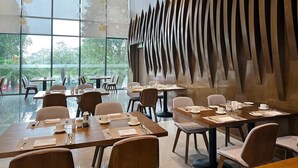 A modern dining area with large windows, wooden tables, and chairs. - DIC Star Hotels & Resorts Vinh Phuc (Vinh Yen)