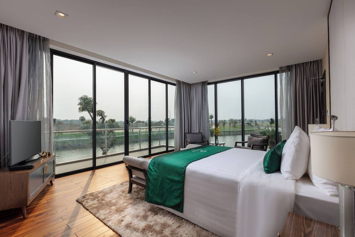 A modern hotel room with a large window, a bed, a TV, and a desk.