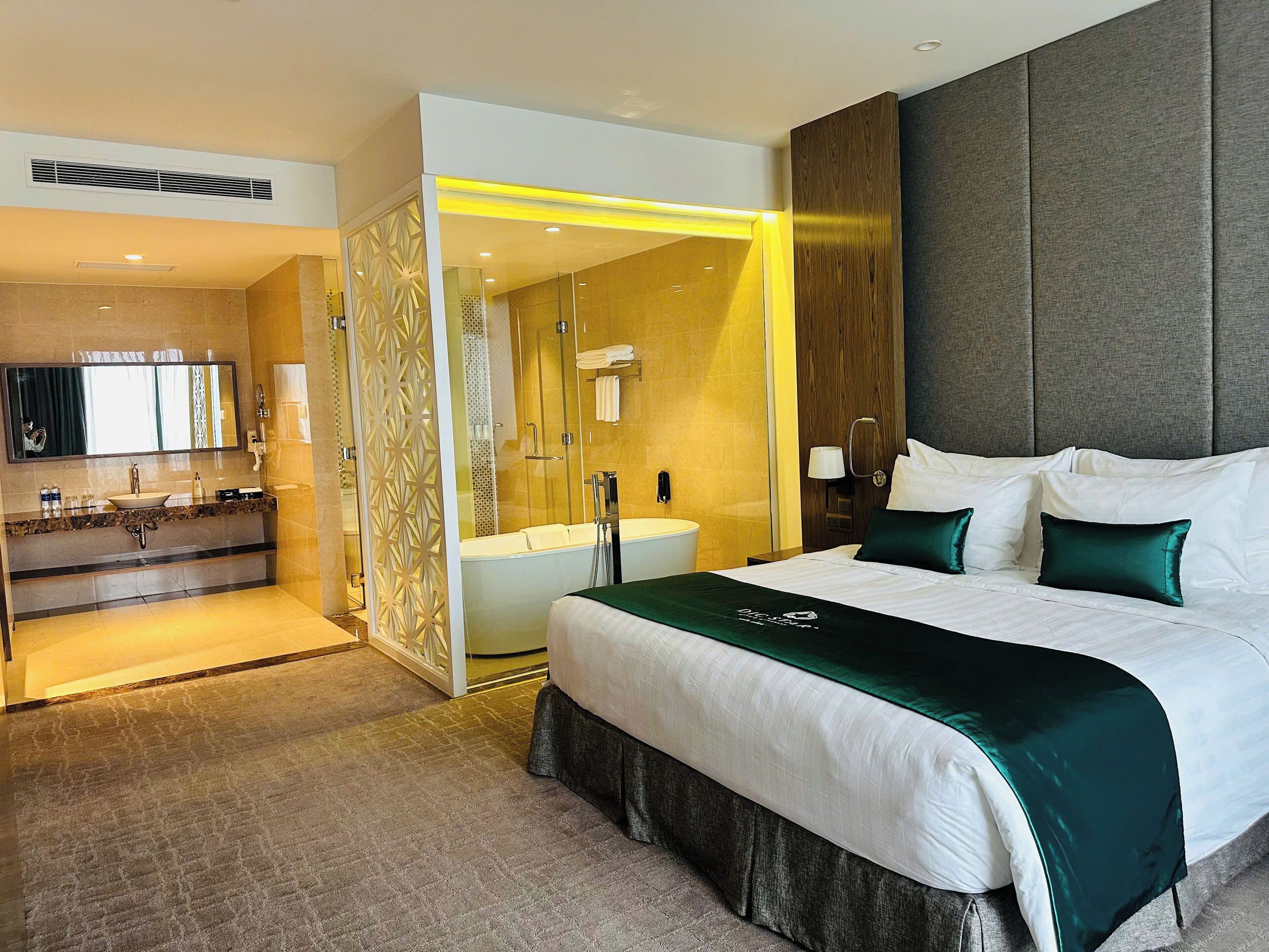 Ein modernes Hotelzimmer mit einem großen Bett, einem separaten Badezimmer mit Badewanne, einem Schminktisch mit Spiegel und einer Duschkabine.