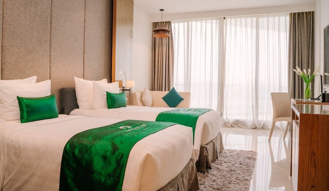 A hotel room with two beds, a desk, and a large window with curtains.