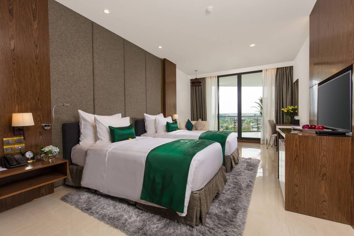 A hotel room with two beds, a desk, a TV, and a large window with a view.