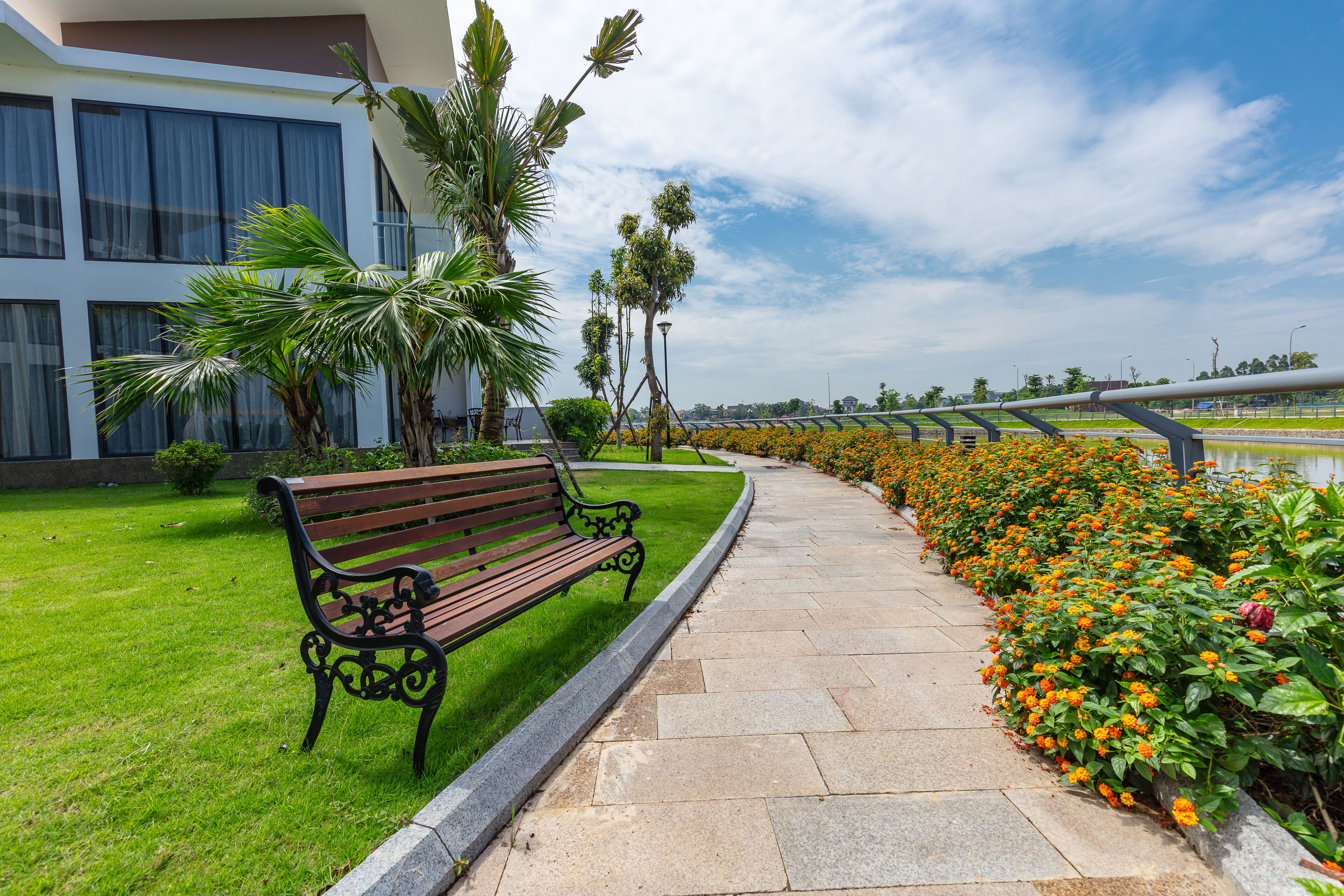 A paved walkway with a bench, bordered by a flower bed and a building with large windows.