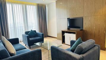 A modern living room with a glass coffee table, two sofas, a flat-screen TV, and wooden paneling.