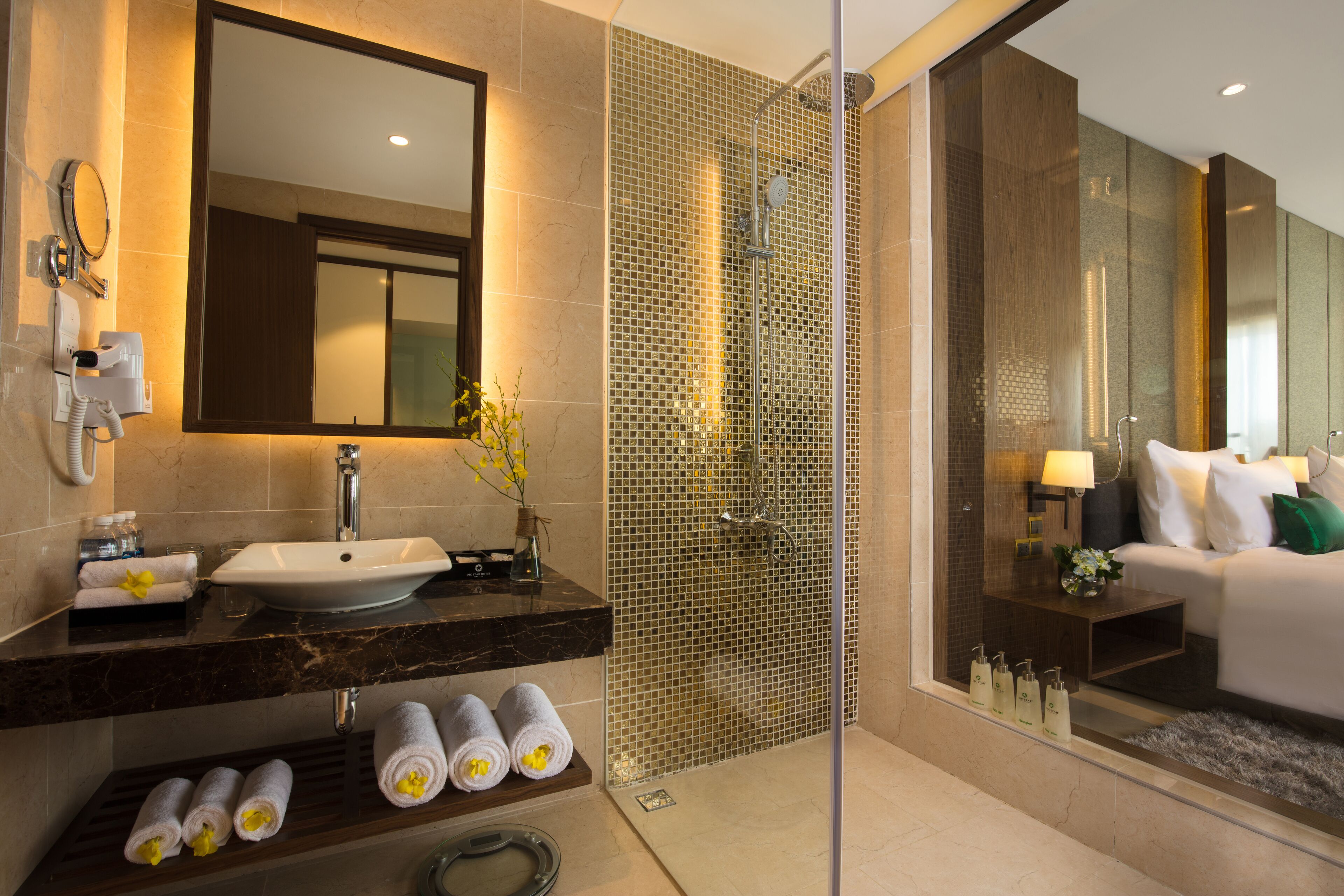 A modern bathroom with a large mirror, a sink, a shower, and a toilet. There are towels and toiletries on the counter.