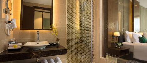 A modern bathroom with a large mirror, a sink, a shower, and a toilet. There are towels and toiletries on the counter.