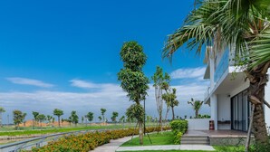 A pathway lined with orange flowers leading to a modern building with a glass facade and a palm tree. - DIC Star Hotels & Resorts Vinh Phuc (Vinh Yen)