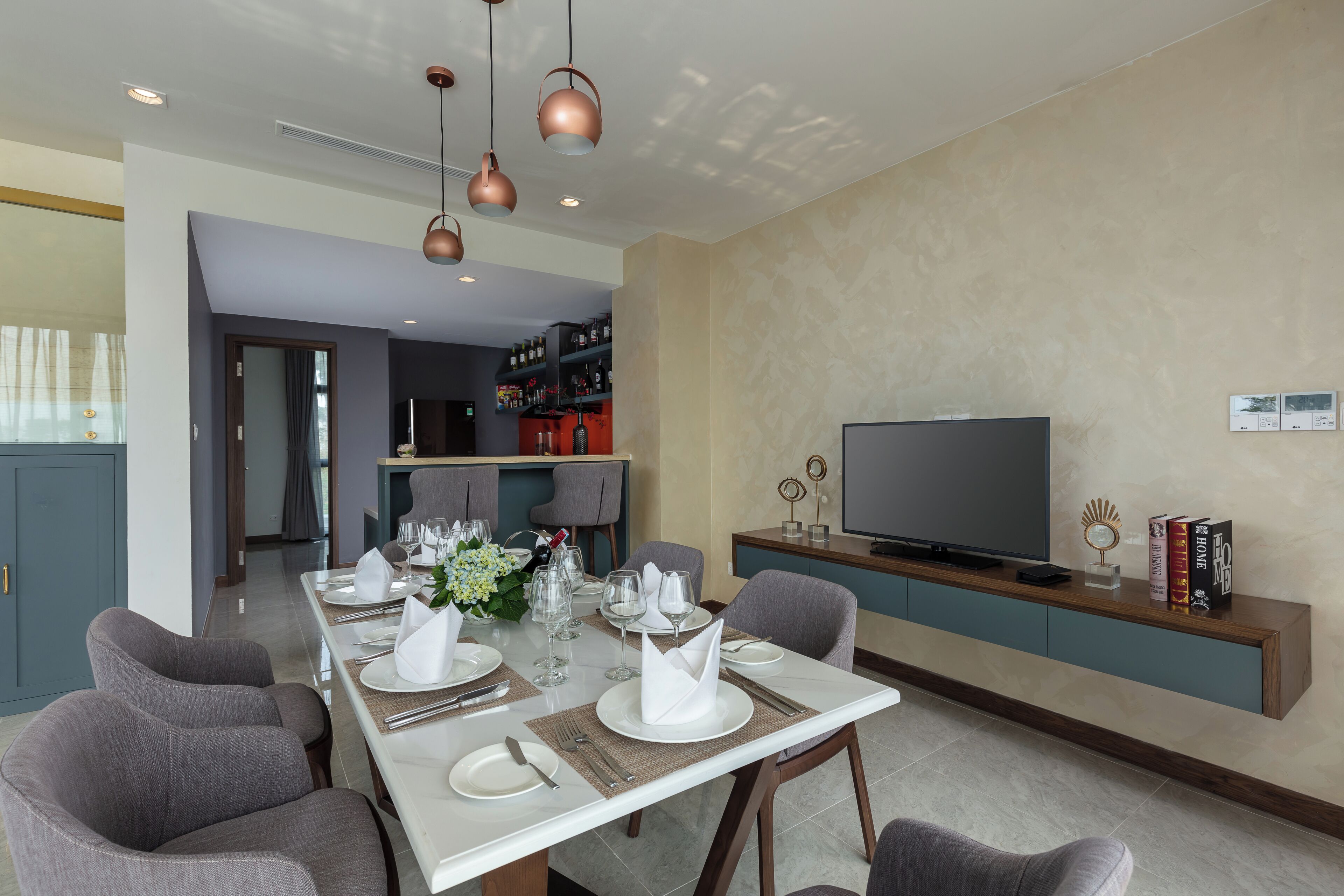 Un comedor con una mesa dispuesta para cuatro personas, un televisor sobre un mueble bajo y una estantería con libros y objetos decorativos.