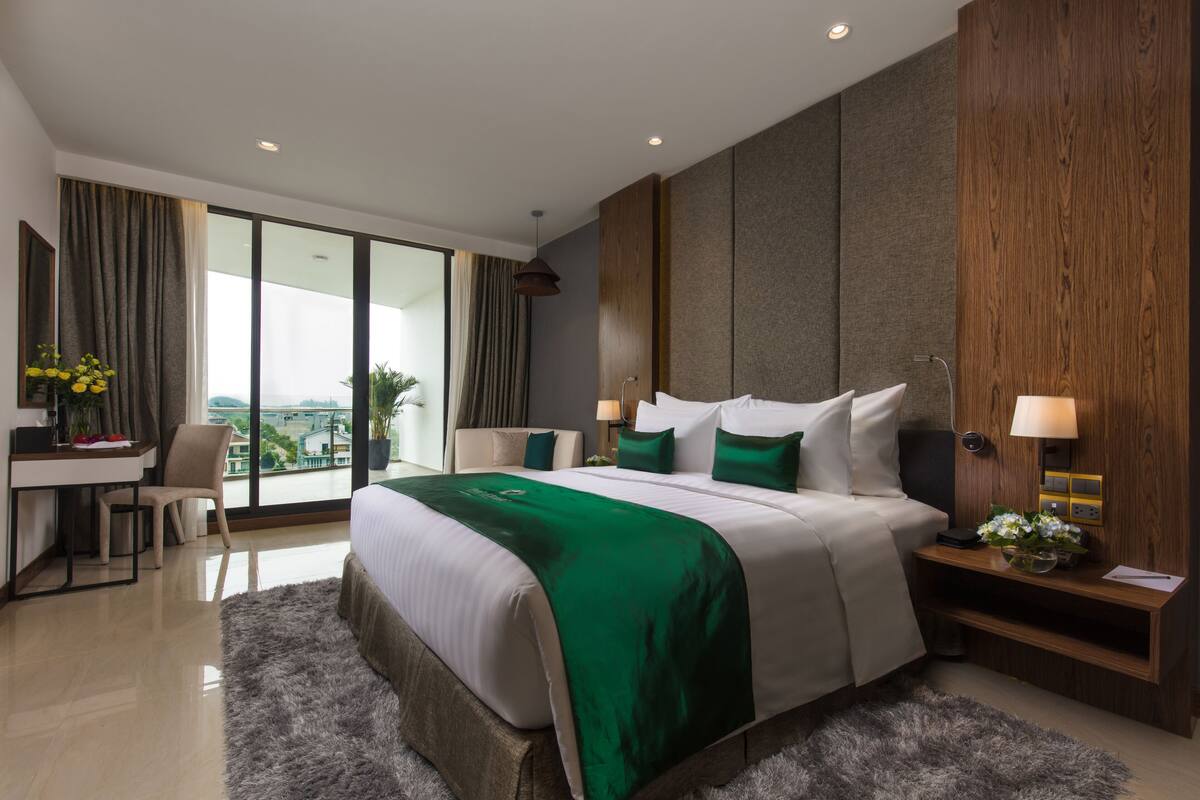 A modern hotel room with a large bed, a desk, and a view of the city.