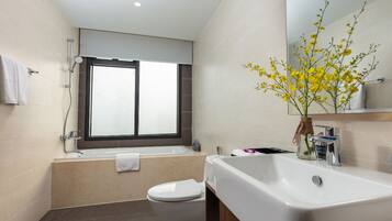 A modern bathroom with a bathtub, toilet, sink, and a window.