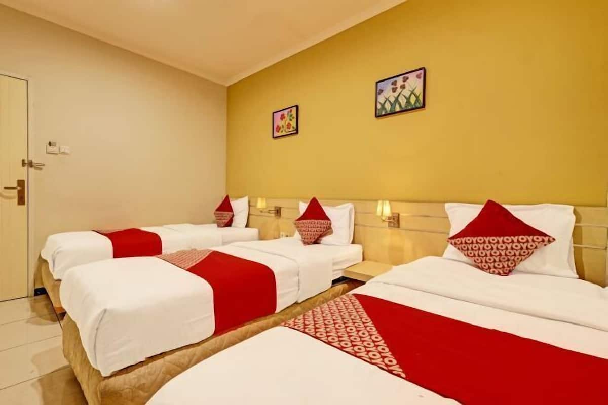 A hotel room with three beds, each with white bedding and red accents, a wooden headboard, and two wall-mounted artworks.