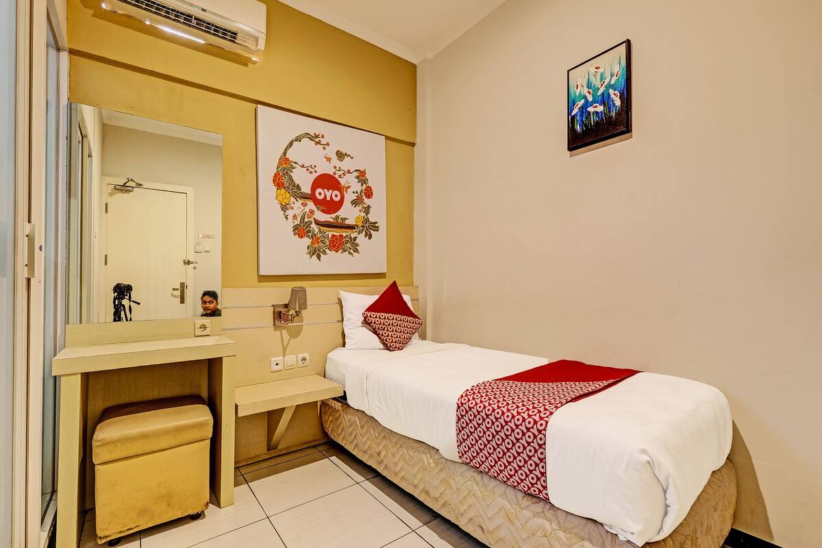 A hotel room with a bed, a bedside table, a mirror, and a wall-mounted air conditioner.
