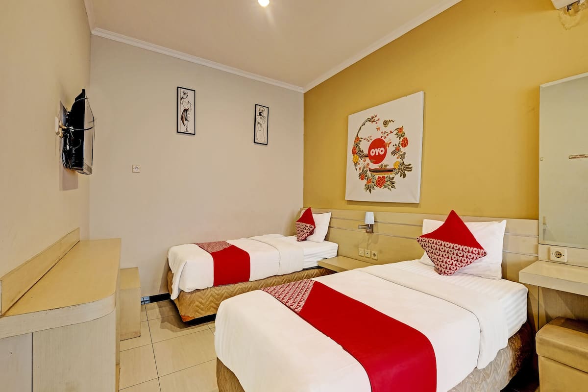 A hotel room with two beds, a mirror, a wall-mounted air conditioner, and a framed artwork.
