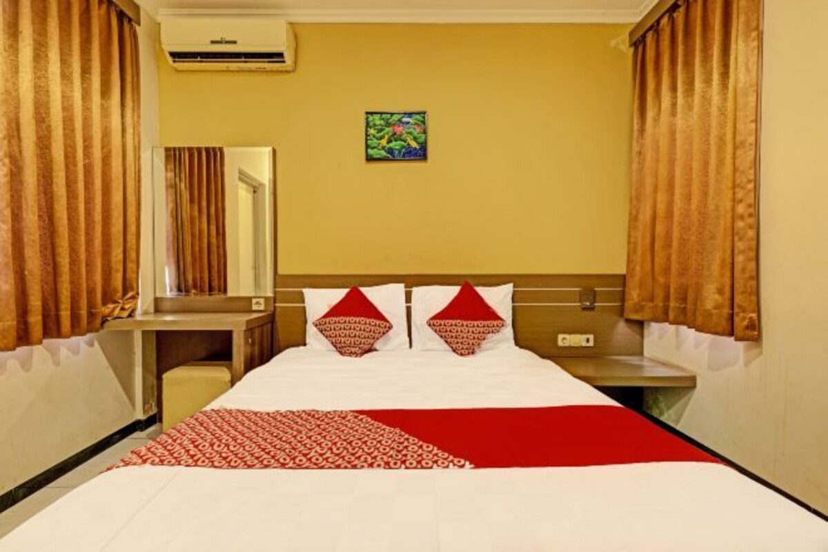 A hotel room with a bed, a bedside table, a mirror, and a painting on the wall.