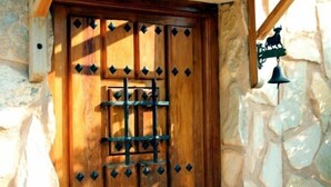 Una puerta de madera con una rejilla metálica y cortes en forma de rombo, en una pared de piedra.