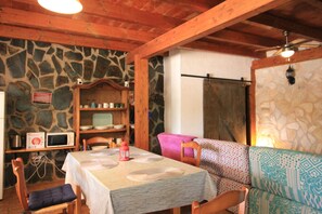 Ein Essbereich mit einem Tisch für zwei Personen, einer Steinwand, Holzbalken, einer Mikrowelle und einem gemusterten Sofa.