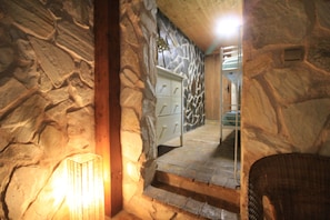 Interno con pareti in pietra, una scala che conduce a una porta, una sedia in vimini e un punto luce a parete.