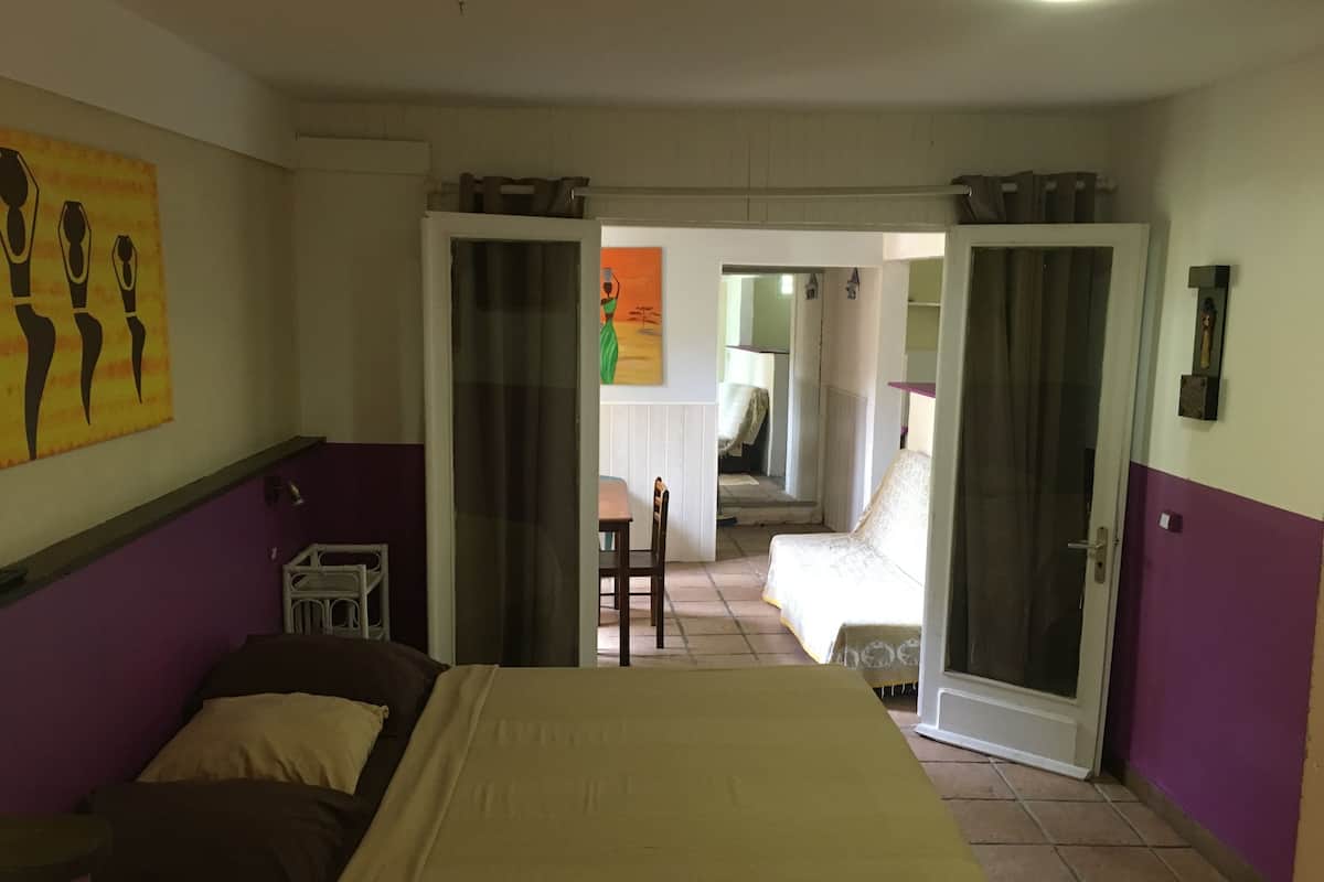 Une chambre d’hôtel avec un lit, une chaise, une petite table et une porte donnant sur une autre pièce.
