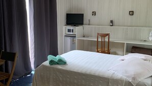 Een hotelkamer met een bed, een bureau met een computer en televisie, een stoel en een bijzettafeltje.