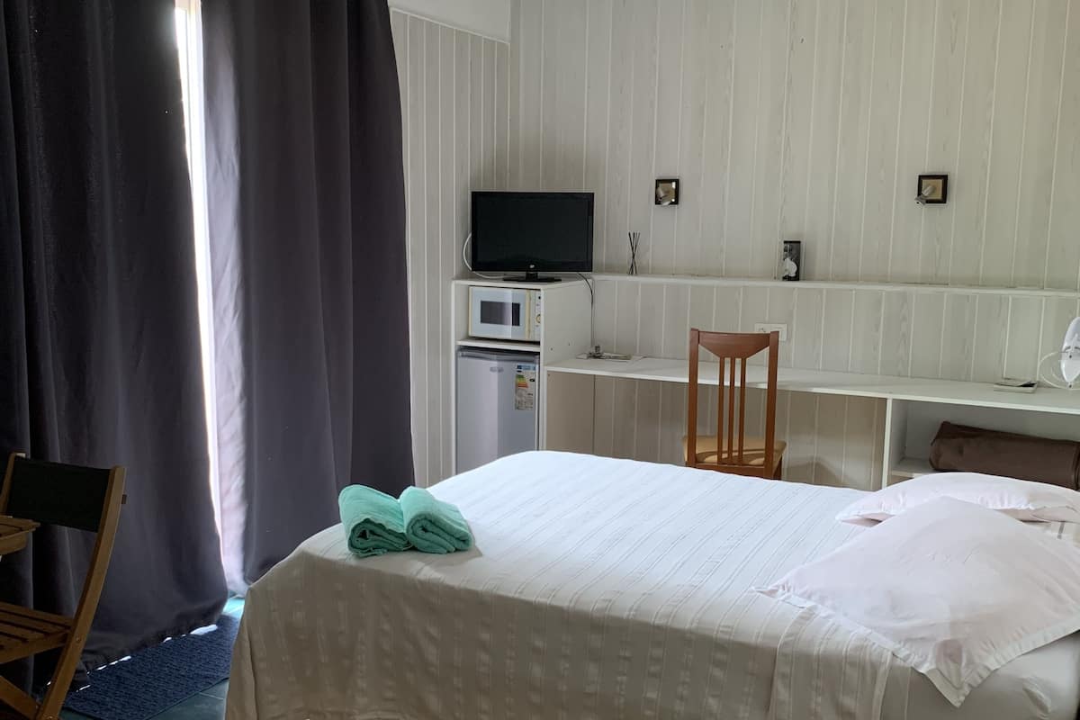 Une chambre d’hôtel comprenant un lit, un bureau avec un ordinateur et une télévision, une chaise et une petite table.