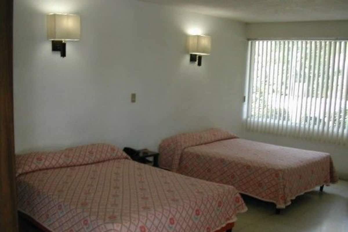 A room with two beds, each with a patterned bedspread, two wall-mounted lamps, and a window with blinds.