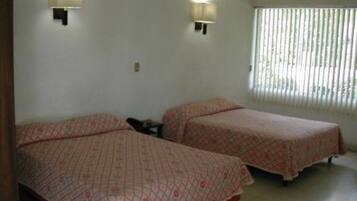 Una habitación con dos camas, cada una con una colcha estampada, dos lámparas de pared y un ventanal con persianas.