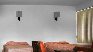 A room with two beds, each with a patterned bedspread, a wooden chair, and two wall-mounted speakers. - Hotel La Jolla (Acapulco)