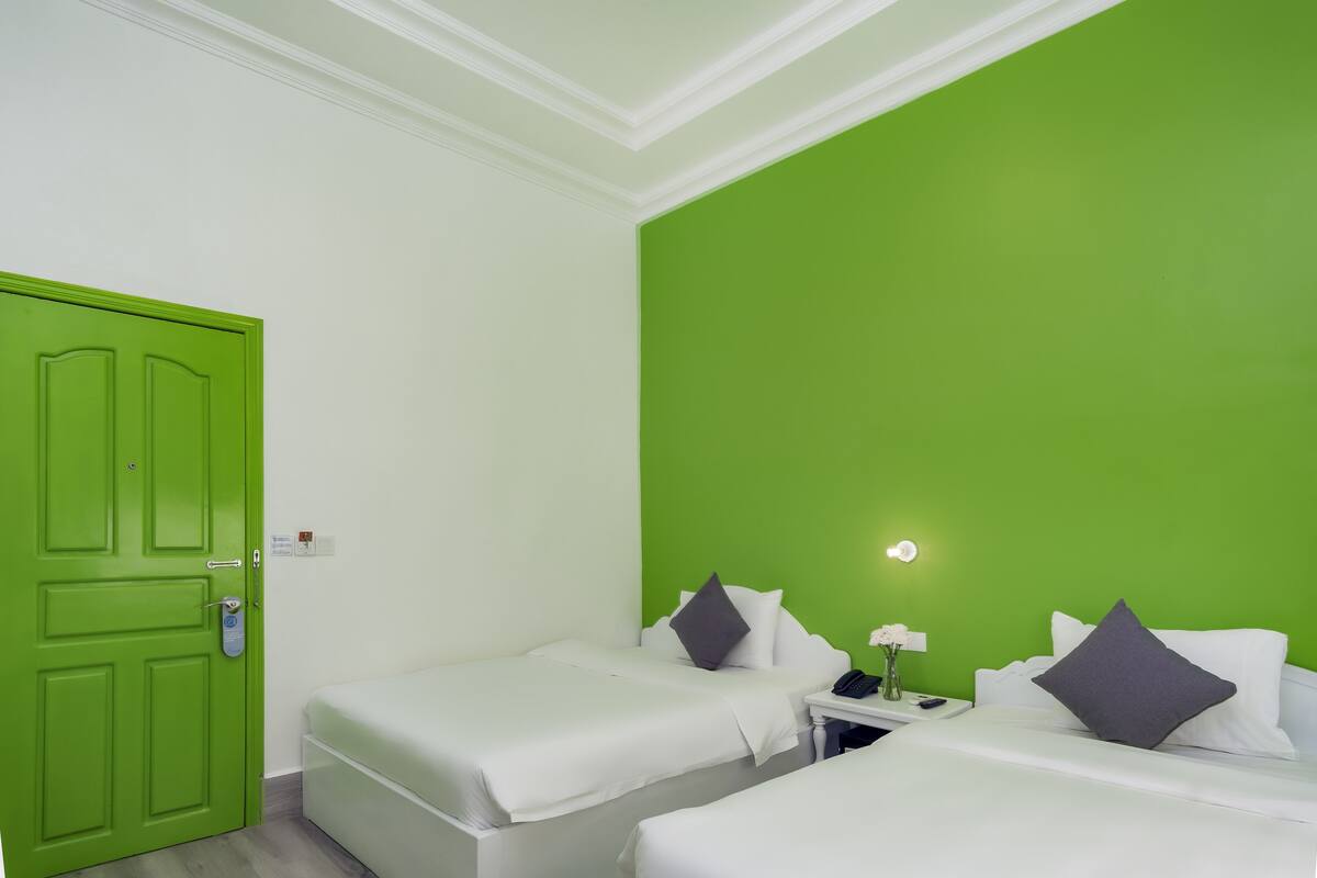 Ein Zimmer mit zwei Betten, einer grünen Tür, einem Nachttisch mit Lampe und einem weiteren Nachttisch mit Telefon.