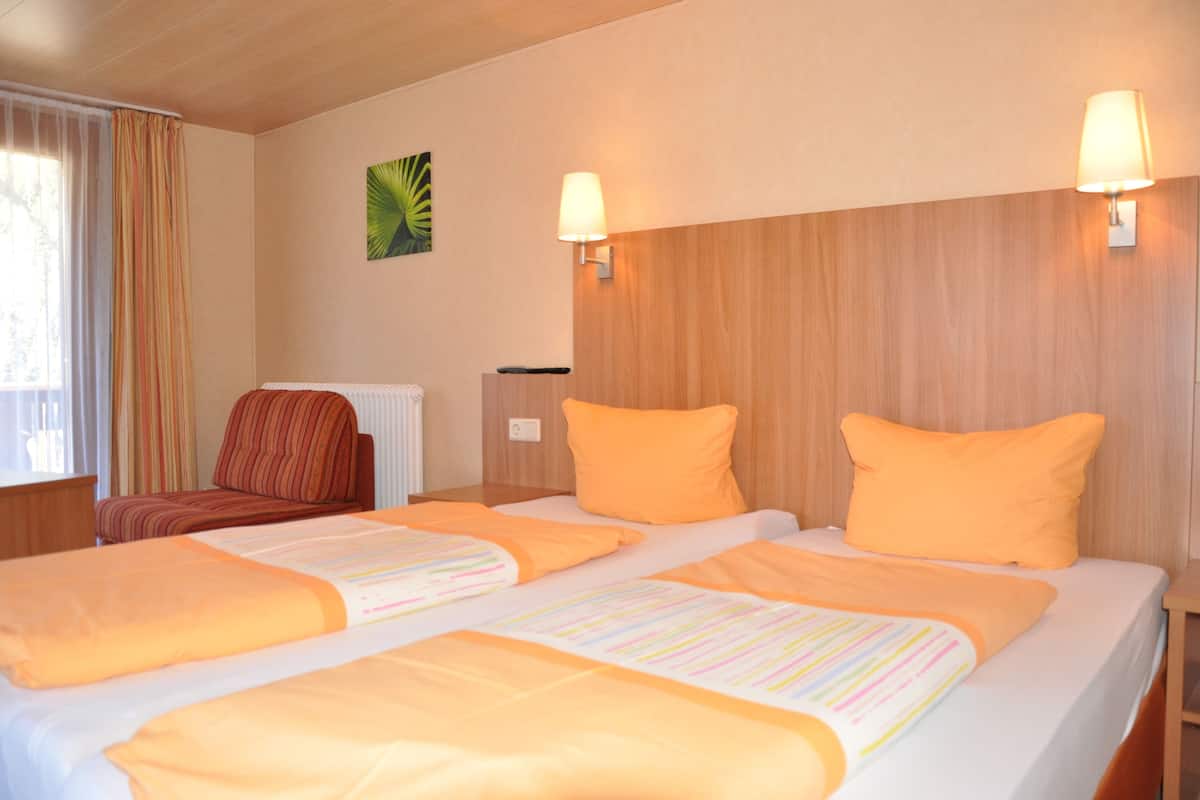 A hotel room with two beds, each with an orange bedspread and pillows, a wooden headboard, and two wall-mounted lamps.