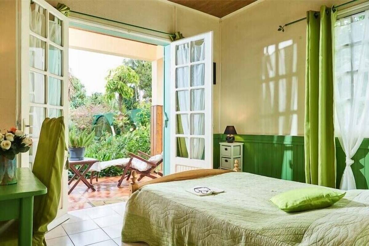 Ein Zimmer mit einem Bett, einem Sessel, einem kleinen Tisch und einem Fenster mit Vorhängen.