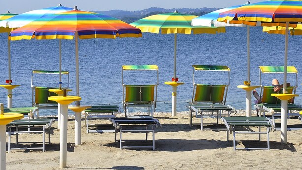 A beach with multiple colorful umbrellas and green lounge chairs. - Albergo Meuble' Olivi (Toscolano Maderno)