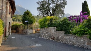 A stone wall with a gate, a clear road, and a mountain in the background. - Albergo Meuble' Olivi (Toscolano Maderno)