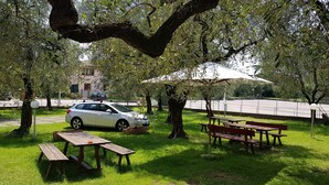 A park with picnic tables, a car, and a white umbrella. - Albergo Meuble' Olivi (Toscolano Maderno)