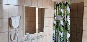 Un baño con teléfono blanco, espejo y cortina de ducha con estampado de hojas.
