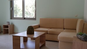 A living room with a beige sofa, a wooden coffee table, and a small shelf with a plant. - Villa Marian (Apokoronas)