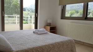 A bedroom with a bed, a window with a view of greenery, a radiator, and a bedside table with a lamp. - Villa Marian (Apokoronas)