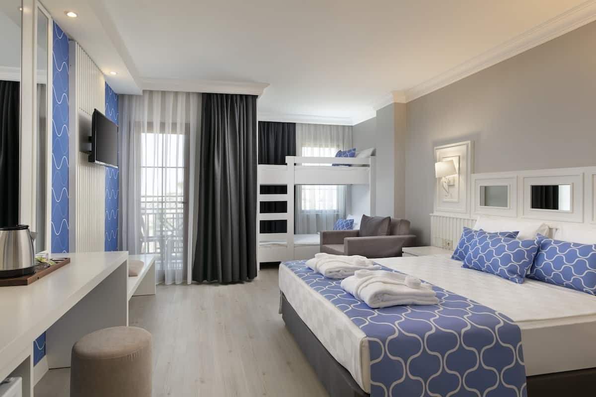 A hotel room with a bed, a desk, a chair, a TV, and a bunk bed.