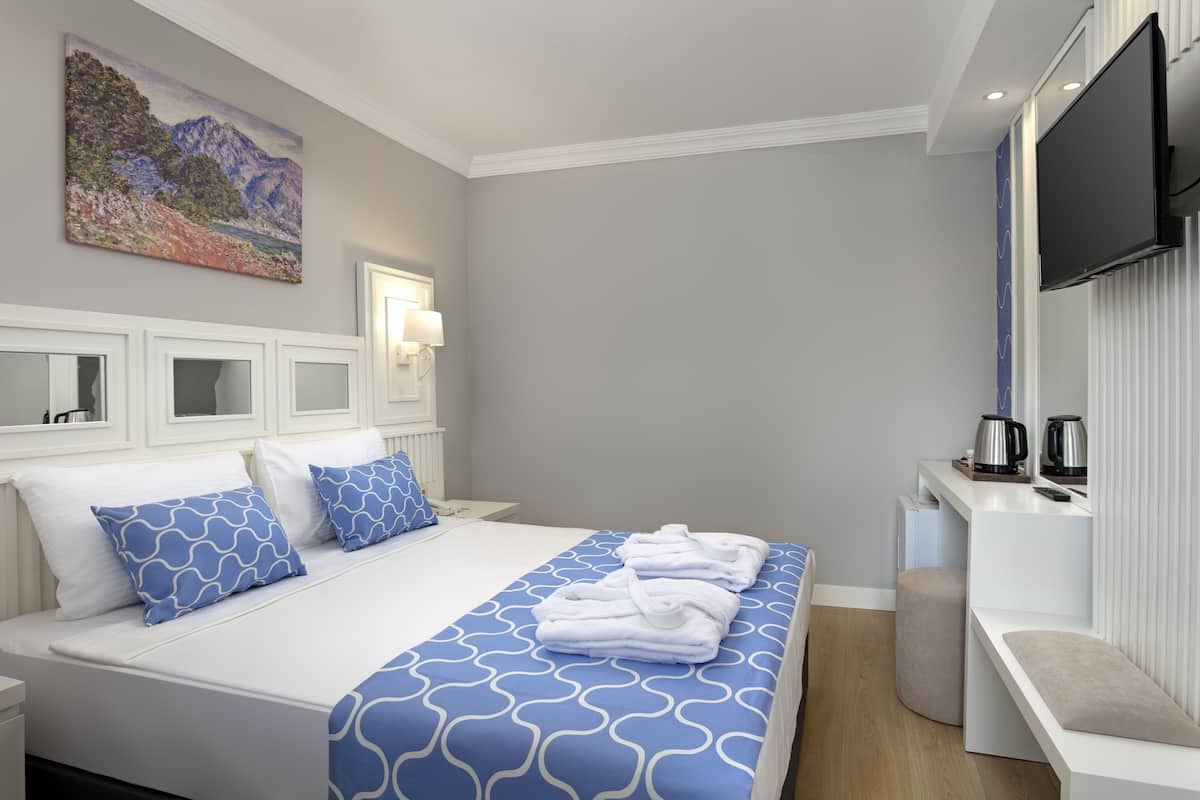 A hotel room with a bed, a bedside table, a TV, and a painting on the wall.