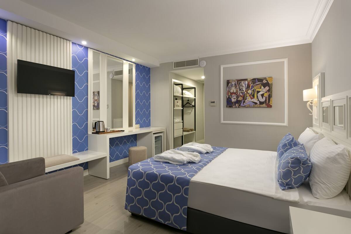 A modern hotel room with a bed, a seating area, a TV, and a bathroom visible through an open door.