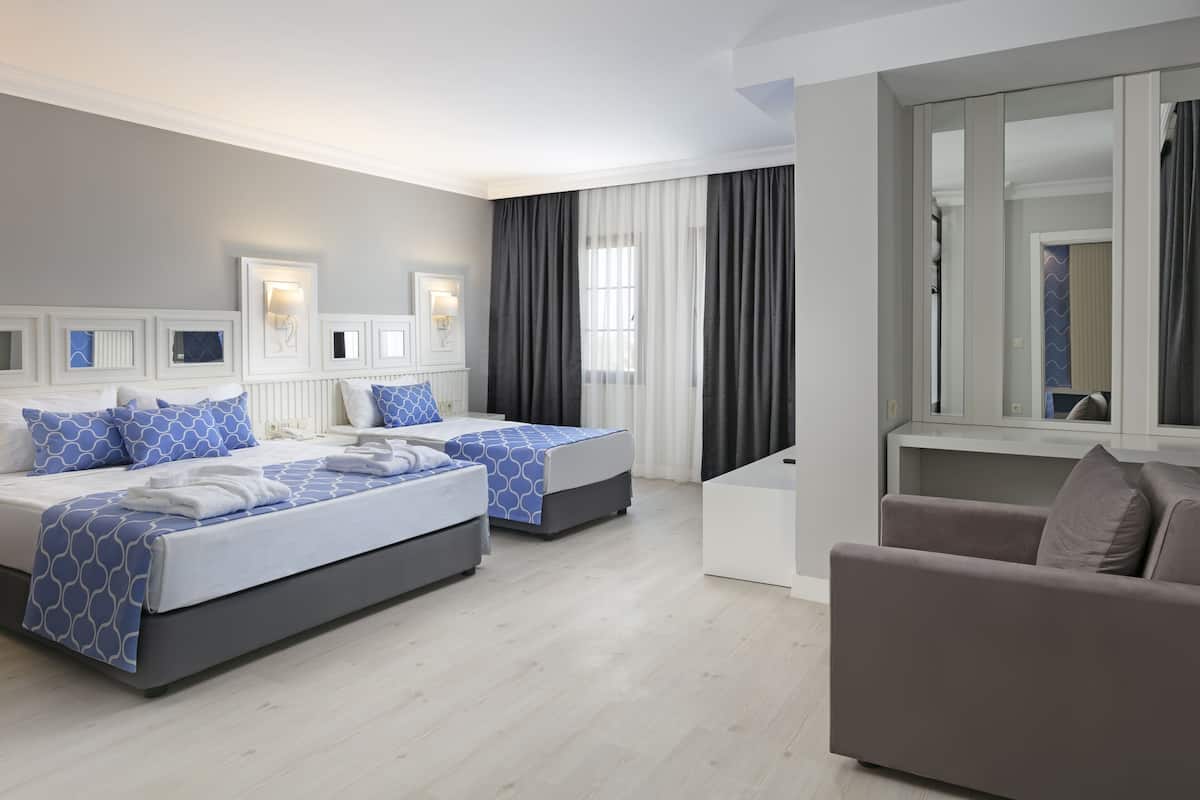 A modern hotel room with two beds, a sofa, and a large mirror.