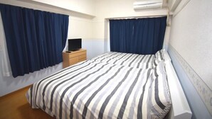Habitación de hotel con cama, mesita de noche, televisor y aire acondicionado.