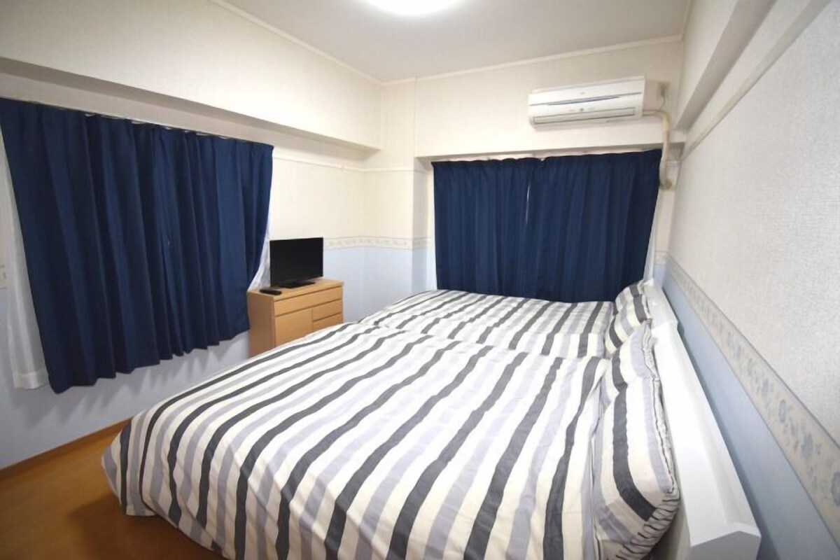 A hotel room with a bed, a nightstand, a TV, and an air conditioning unit.