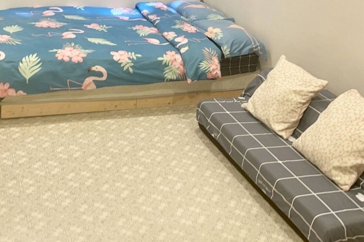 A bedroom with a bed, a sofa, a window with curtains, and an air conditioning unit.